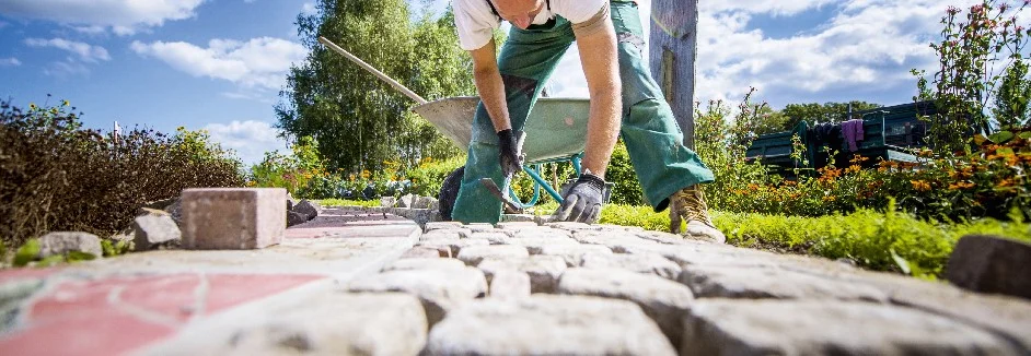 Person verlegt Pflastersteine mit Gummihammer